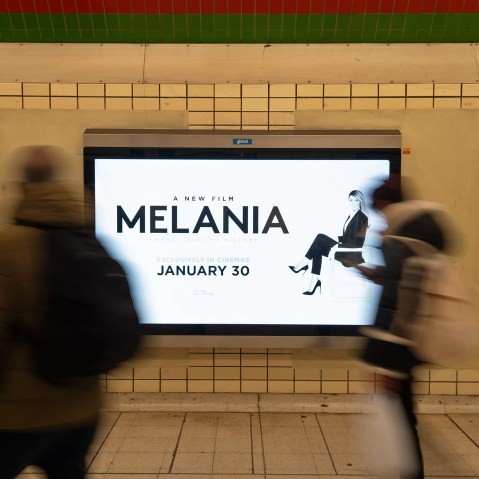 People, blurred in motion, walk past an advertisement for the movie "Melania."