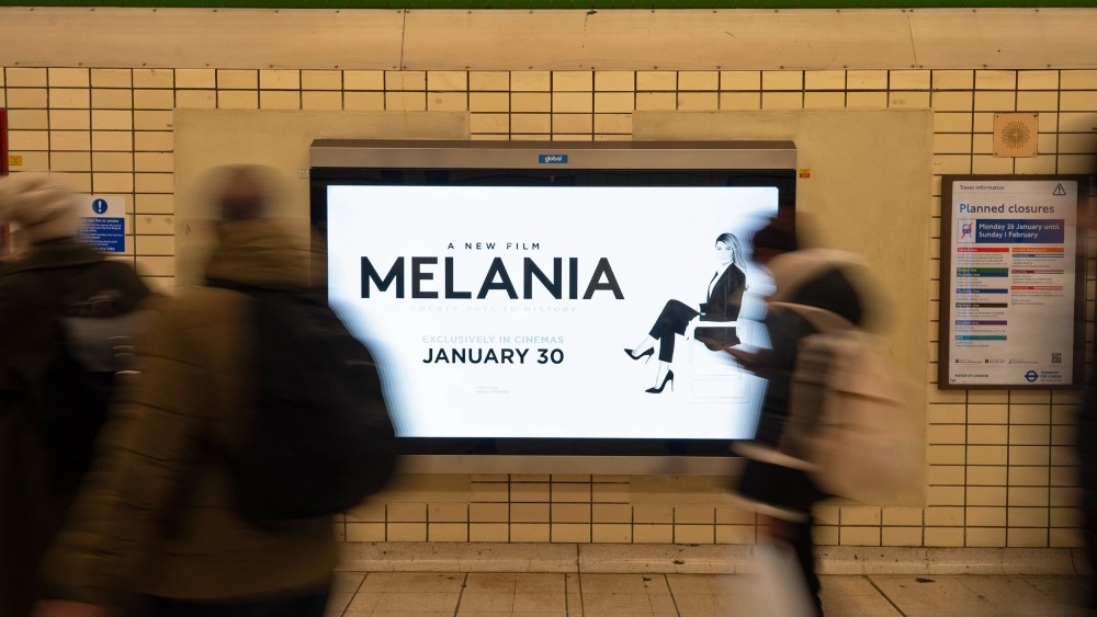 People, blurred in motion, walk past an advertisement for the movie "Melania."