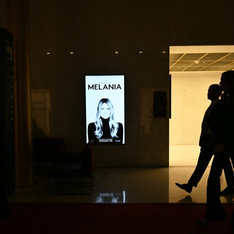 Silhouettes walk past a poster for "Melania."