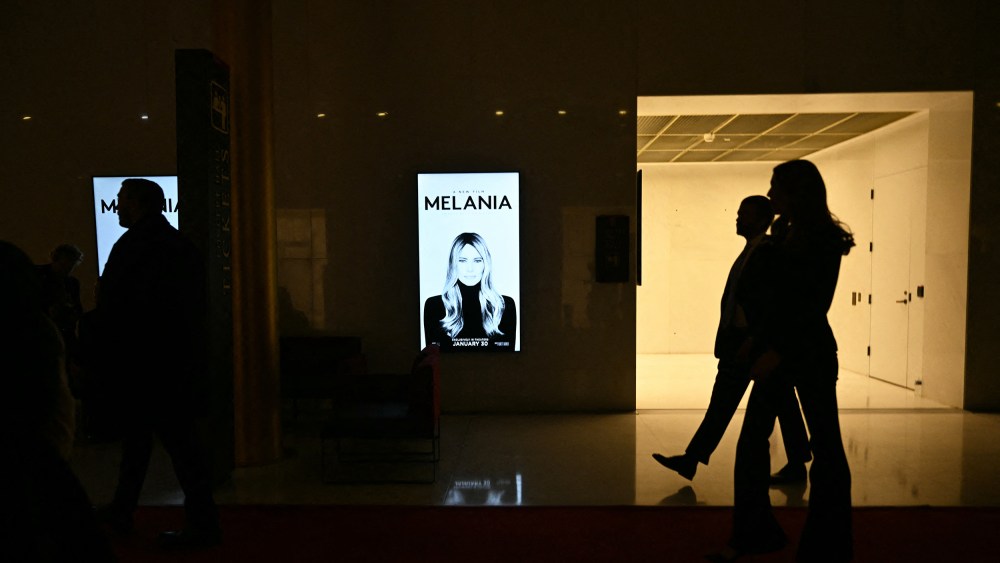 Silhouettes walk past a poster for "Melania."