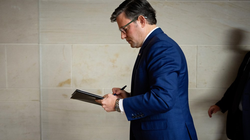 Mike Johnson, facing left, walks while writing on a piece of paper.