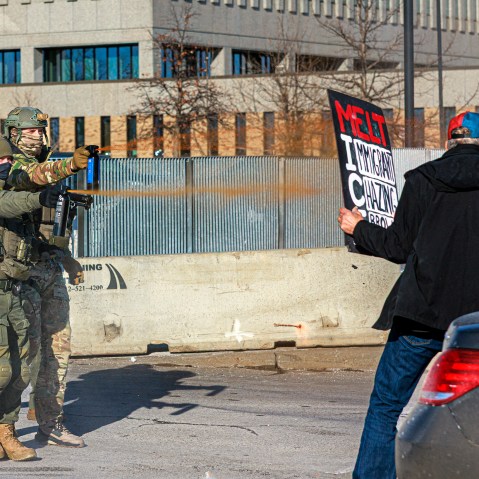 Federal agents use pepper spray against a protester holding a sign during an enforcement operation outside the Whipple Building in Minneapolis.