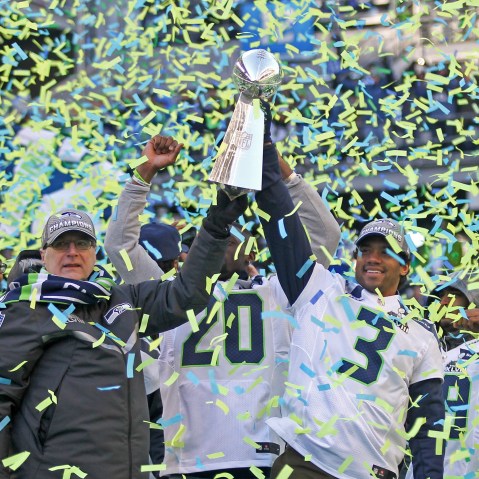 Paul Allen, left, and Russell Wilson hoist the Lombardi trophy in the air as blue and green confetti falls around them.