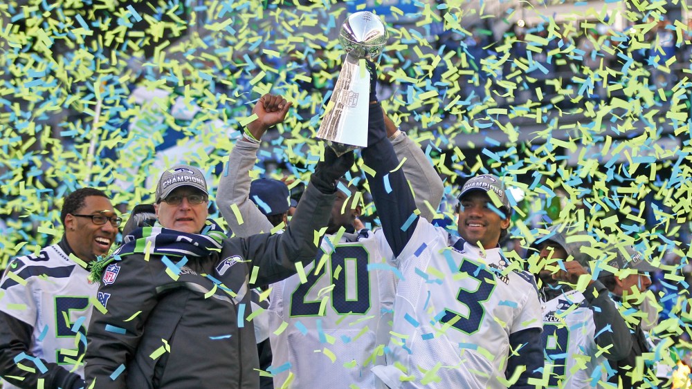 Paul Allen, left, and Russell Wilson hoist the Lombardi trophy in the air as blue and green confetti falls around them.