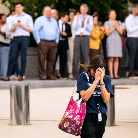 A person walks away with their head in their hands as people out of focus behind them clap and film.