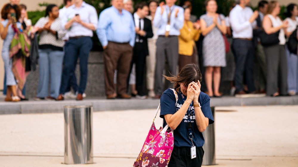 A person walks away with their head in their hands as people out of focus behind them clap and film.