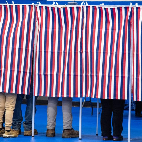 Legs are seen below red, white and blue voting booth curtains.