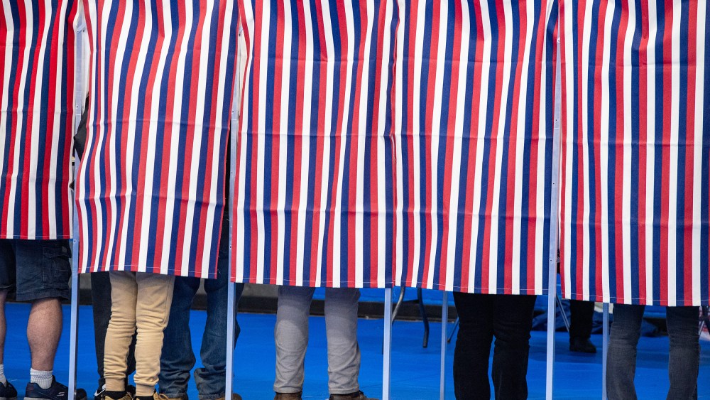 Legs are seen below red, white and blue voting booth curtains.