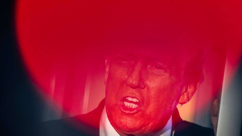 Top part of Donald Trump's face is seen through a round red light.
