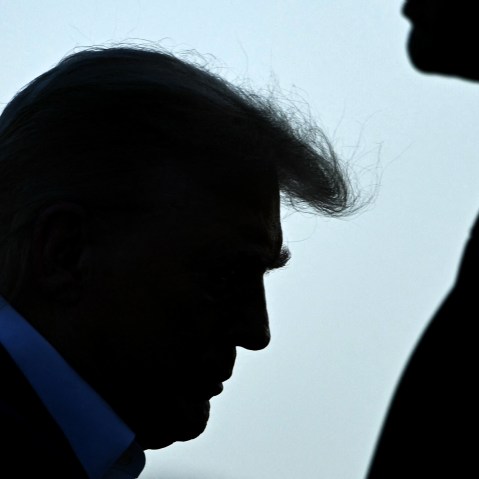Trump's profile is seen as he walks up to the place. A security person stands on the right side.