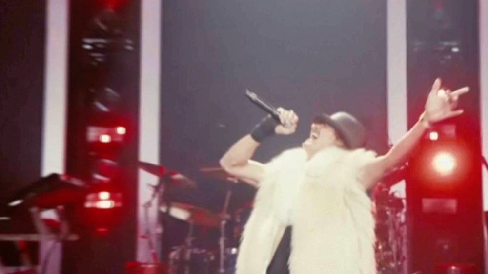 Kid Rock wearing a white west while he sings on stage.