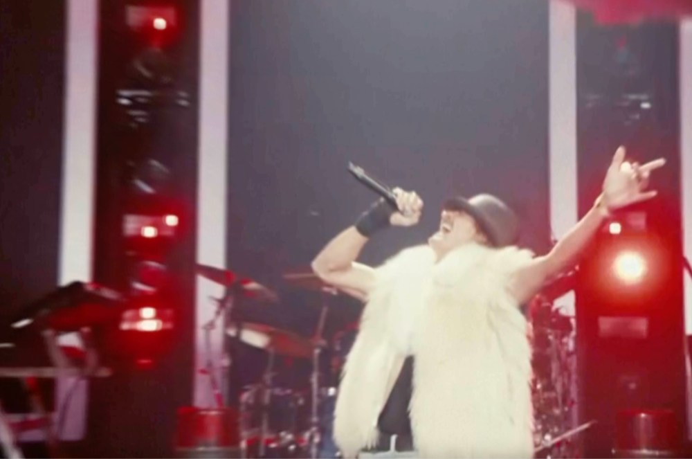 Kid Rock wearing a white west while he sings on stage.