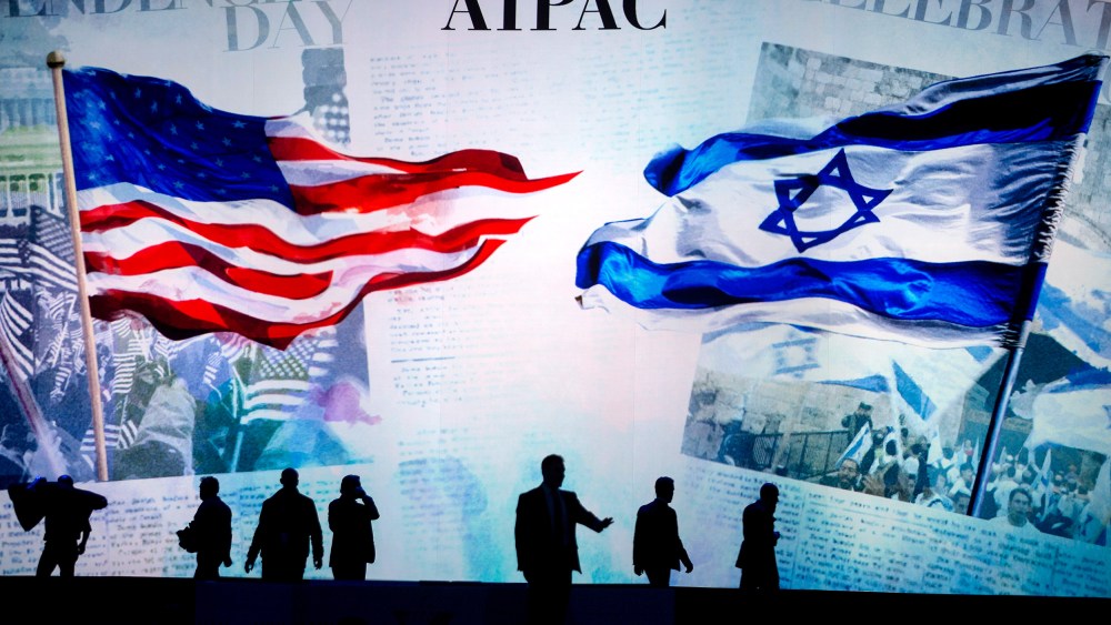 People are silhouetted before a screen that reads "AIPAC" and shows a visual of the American flag and the Israeli flag.