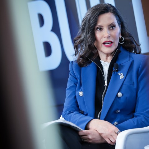 Gretchen Whitmer sits at the stage, seen through two lines.
