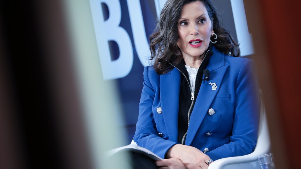 Gretchen Whitmer sits at the stage, seen through two lines.