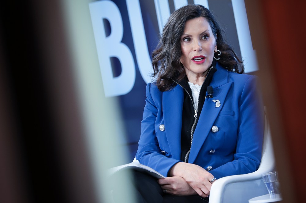 Gretchen Whitmer sits at the stage, seen through two lines.