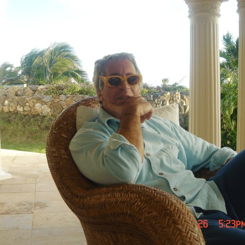 Jeffrey Epstein sits at a patio wearing yellow framed sunglasses.