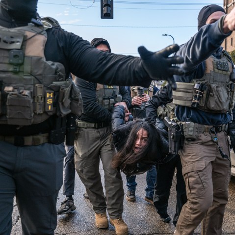Federal agents hold a person by their arms and legs in the street.
