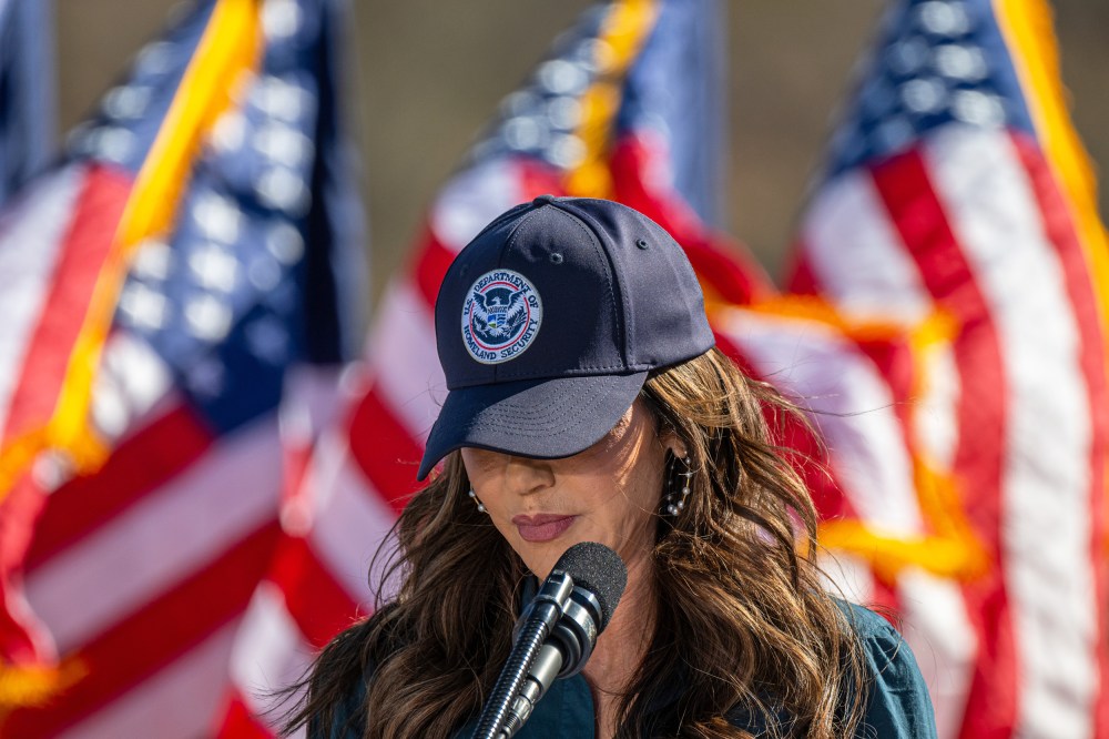 Kristi Noem with her head tilted down, her "U.S. Department of Homeland Security" baseball cap obscuring her eyes.