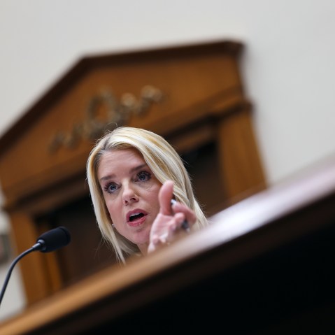 Pam Bondi behind a microphone, partially obscured by the desk in front of her.