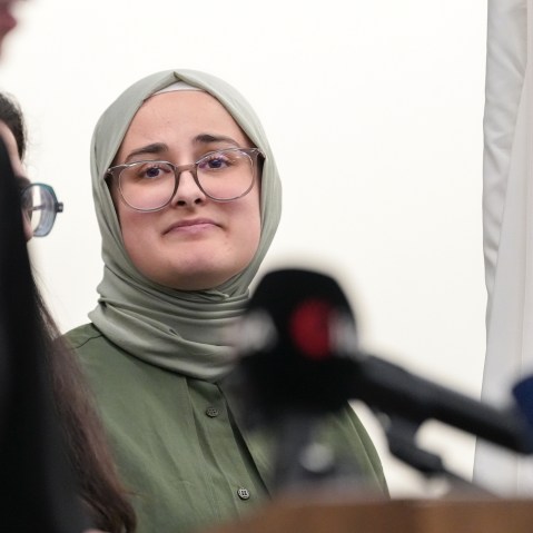 Rumeysa Ozturk looks at the woman speaking at the podium.
