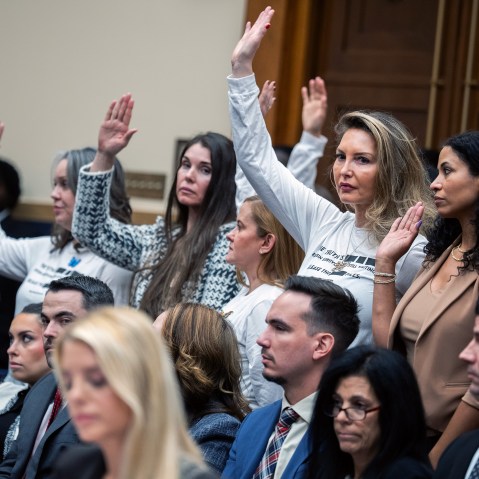 People in focus in the background raise their hands; Pam Bondi out of focus in the foreground looks down.
