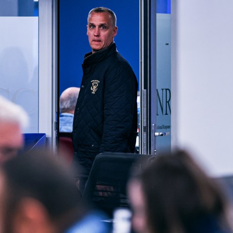 Corey Lewandowski stands in a doorway. Blurred in the foreground, people work at their desks.