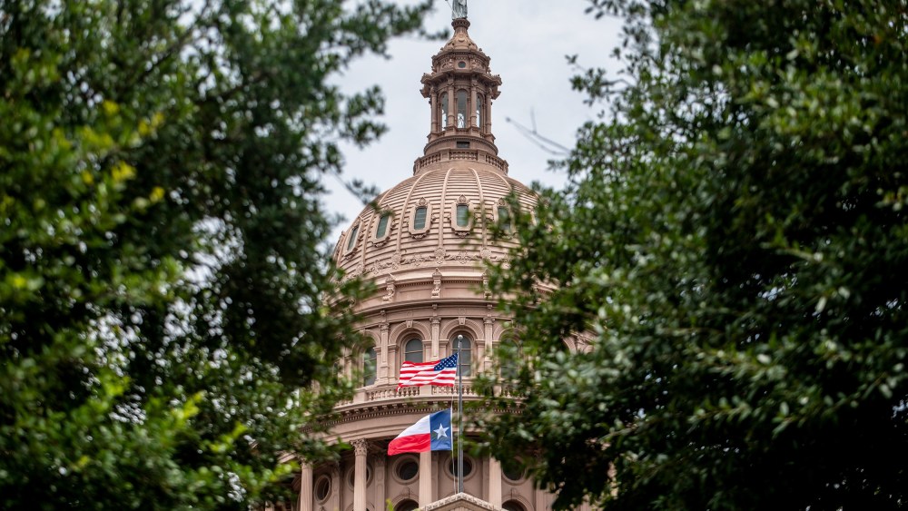 The Texas State Capitol dome peeks out from behind two trees.