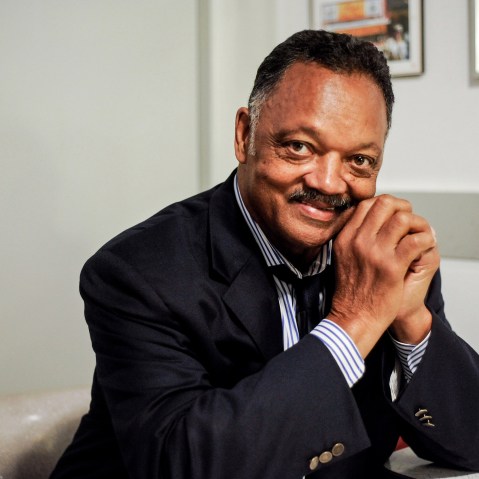 Rev. Jesse Jackson poses for a portrait, sitting down with his hands clasped up by his face.