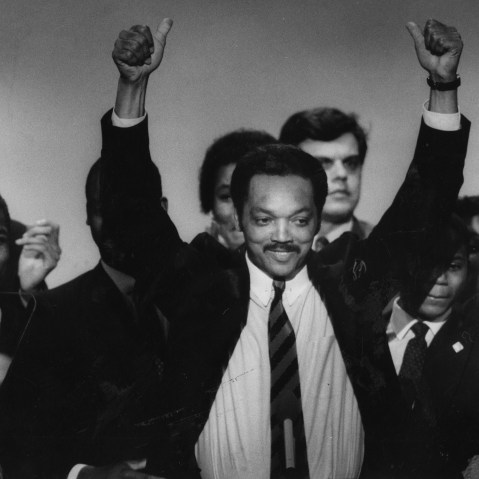 Jesse Jackson Sr. lifts his arms surrounded by a group of people mixed-aged people.