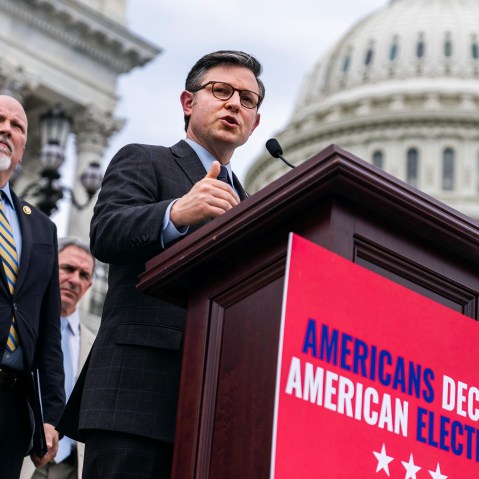 Mike Johnson, right, and Rep. Chip Roy at a podium in front of the Capitol. The podium has a red sign that says "Americans decide American elections."