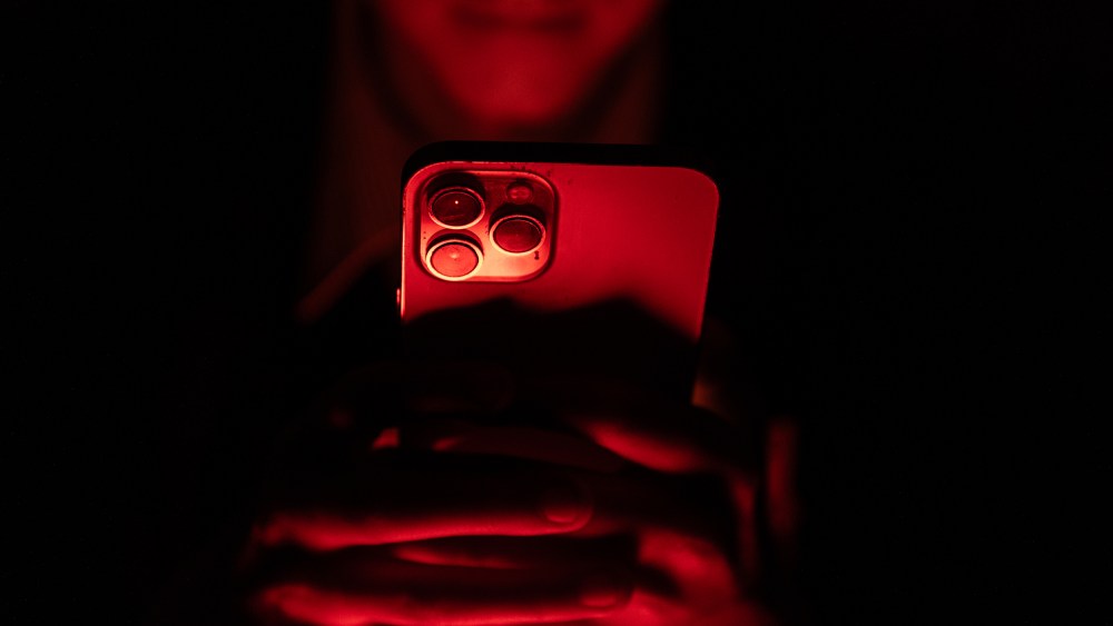 A person's hands hold an iPhone. The scene is bathed in a red light.