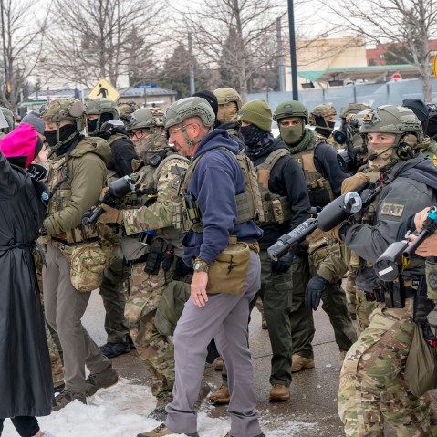There is one single protestor wearing a a pin k hat in the left side of the frame confronting a large number of federal agents.