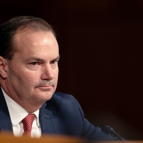 Mike Lee looks on during a hearing. The background is completely black.