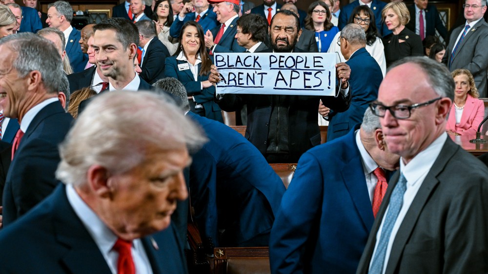 Al Green holds a sign that says "Black People Aren't Apes!" In the foreground, President Trump is visible but out of focus.