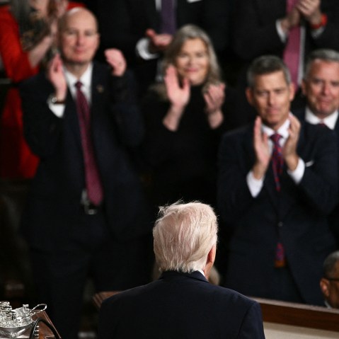 People clap, out of focus, as the back of Donald Trump's head is seen in focus in the foreground.