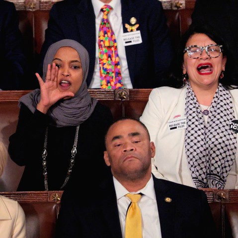 Ilhan Omar has her hand around his mouth as she and Tlaid yells.