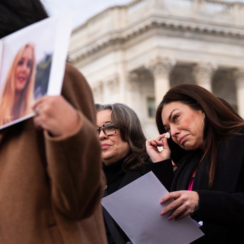 Epstein survivor Haley Robson, second from right, wipes tears from her eyes with tissue. She is surrounded by people, including other survivors.