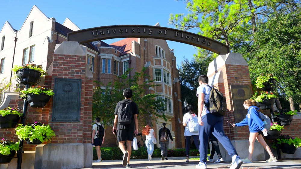 Students walk under the arch of University of Florida entrance on a sunny day.