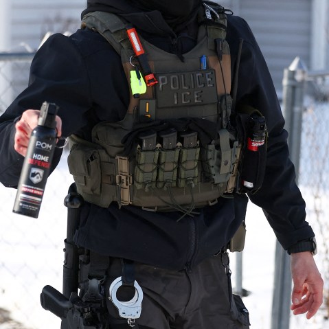 Torso of an ICE agent is seen as he aims a pepper spray canister forward.