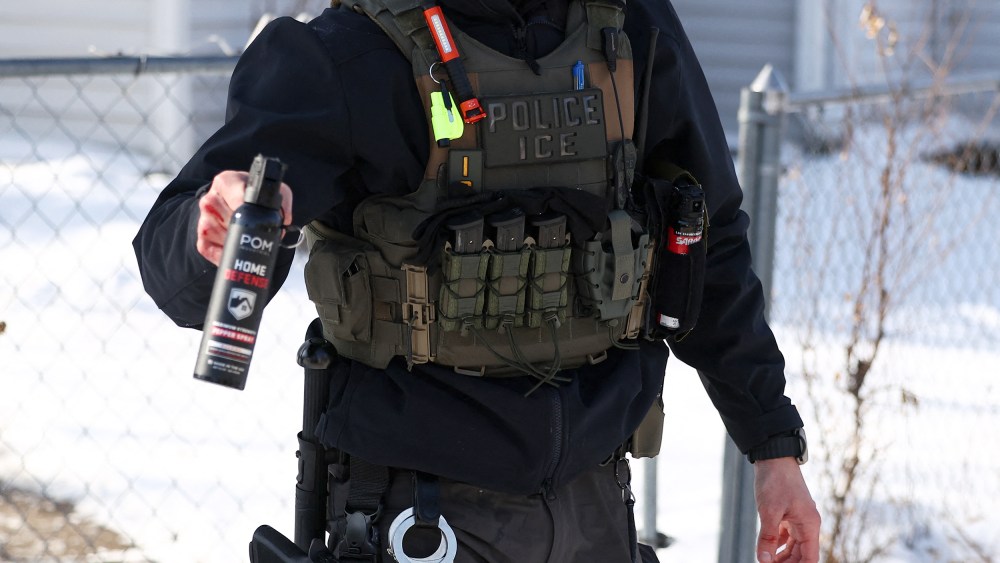 Torso of an ICE agent is seen as he aims a pepper spray canister forward.