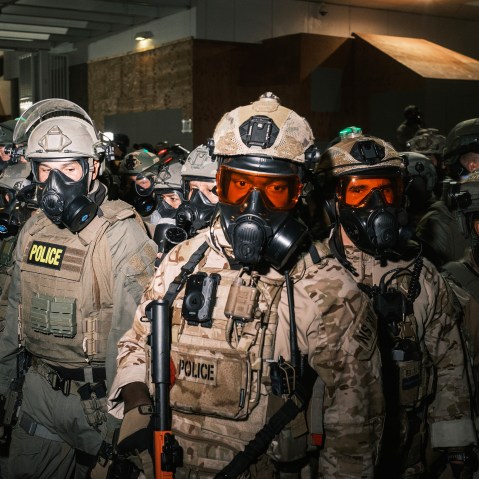 A crowd of federal officers in gas masks and helmets.