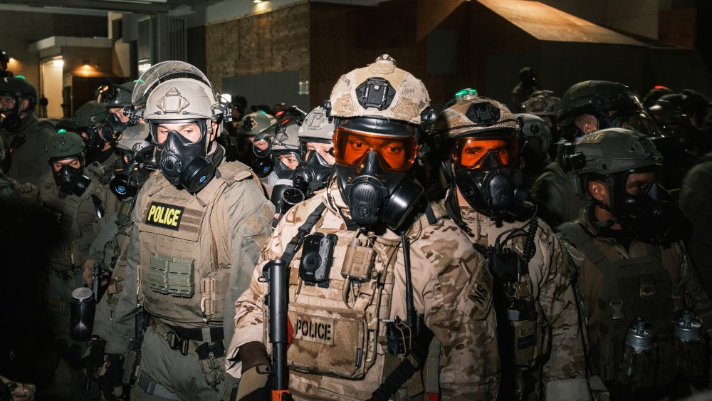 A crowd of federal officers in gas masks and helmets.