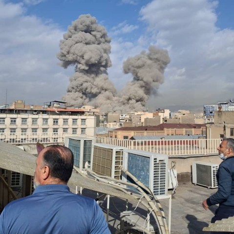 Men standing on rooftops look on at clouds of smoke rise from US airstrikes