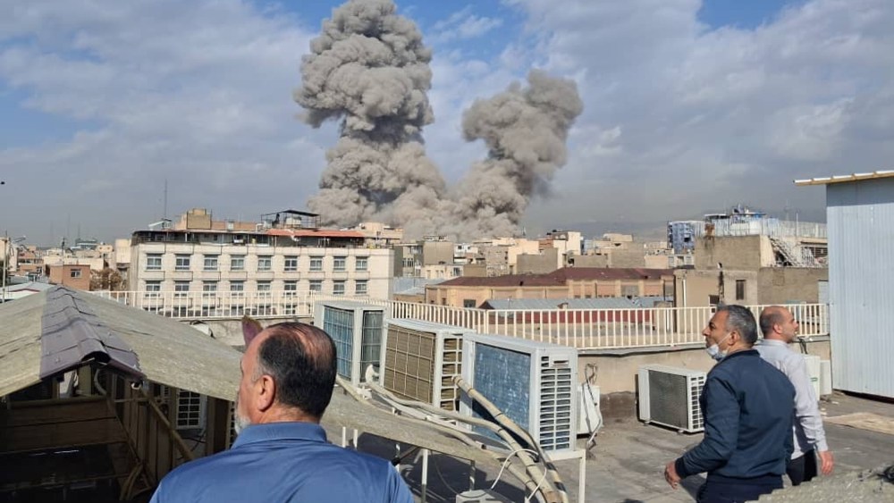 Men standing on rooftops look on at clouds of smoke rise from US airstrikes
