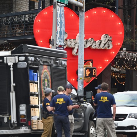 People wearing shirts that say "FBI" stand by an FBI truck outside of a bar. The front entrance of the bar is decorated with a big red heart that has the name "Buford's" in cursive in the center.