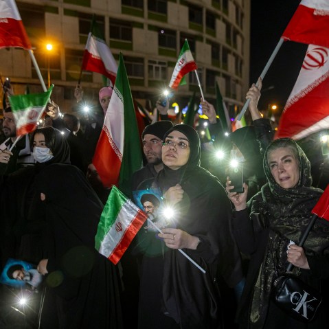 A crowd of people hold pictures of Ayatollah Ali Khamenei and wave Iranian flags.