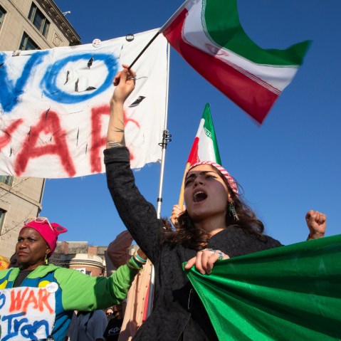 People wave Iranian flags and hold signs that say "NO WAR" and "NO WAR with Iran."