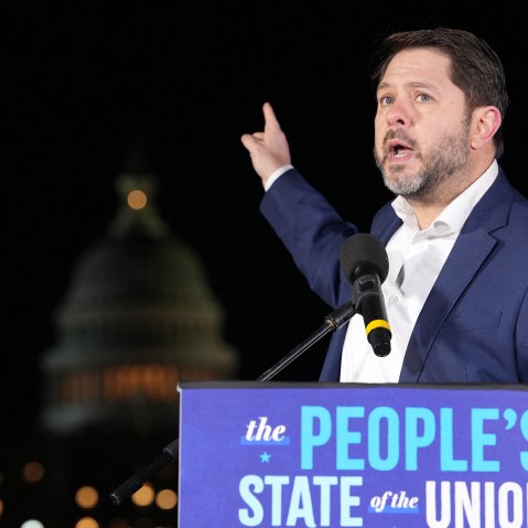 Ruben Gallego points at the capitol building as he speaks outside at night.