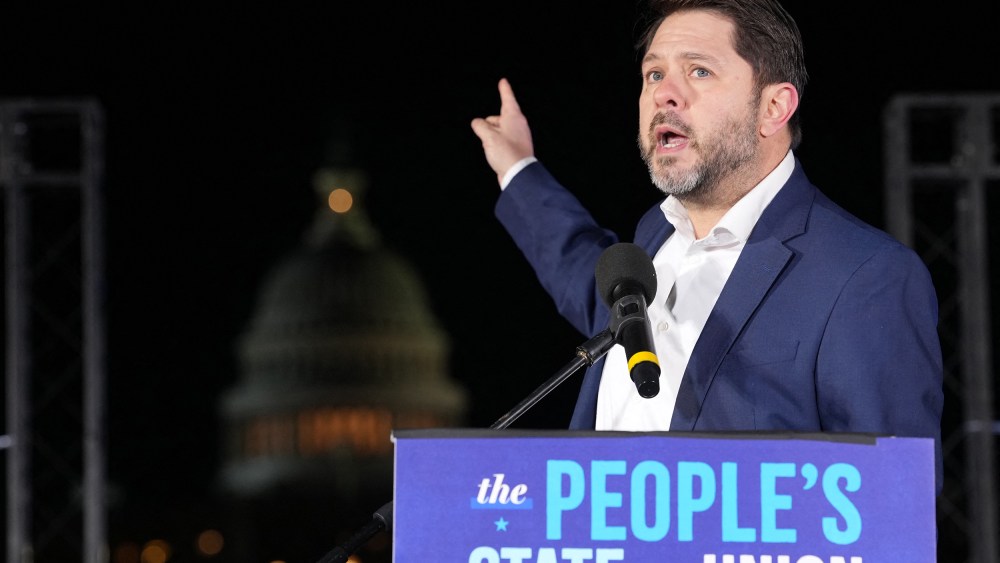 Ruben Gallego points at the capitol building as he speaks outside at night.